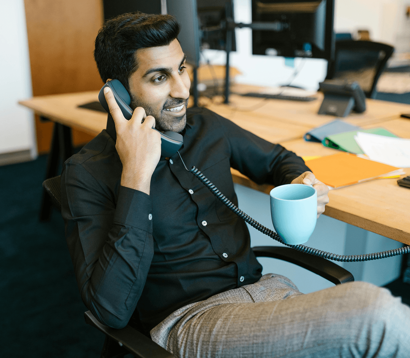 Man talking on office phone holding coffee